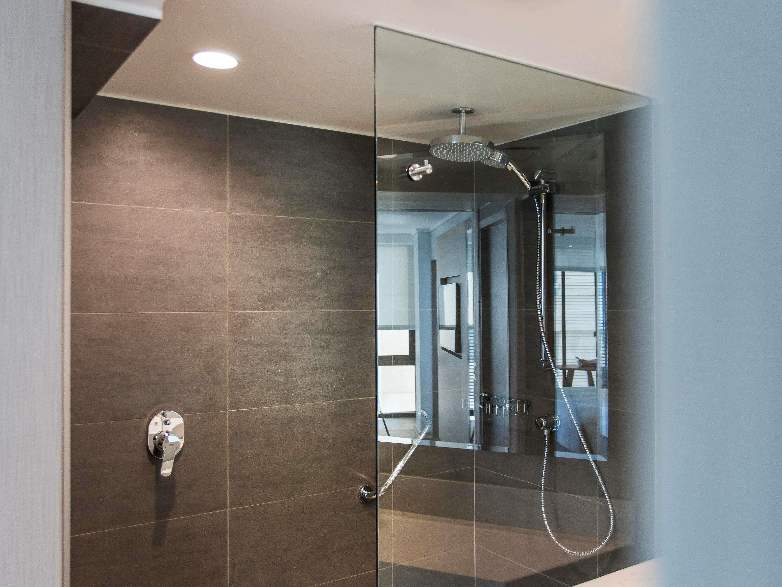 Ducha moderna con separador de vidrio, panel de control visible y vista despejada al baño contiguo.