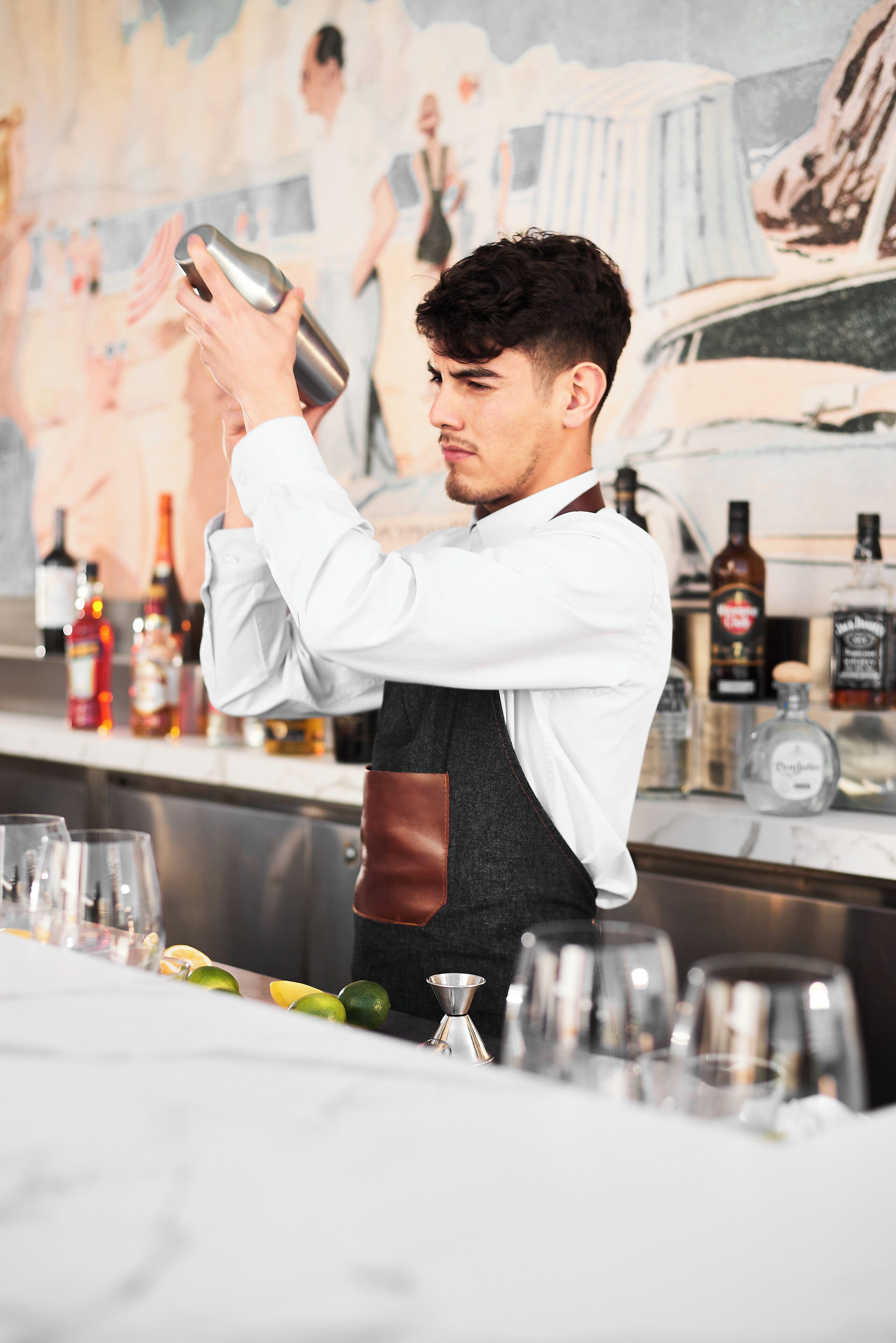 Un bartender preparando bebidas en una barra, con una variedad de botellas y vasos al fondo.