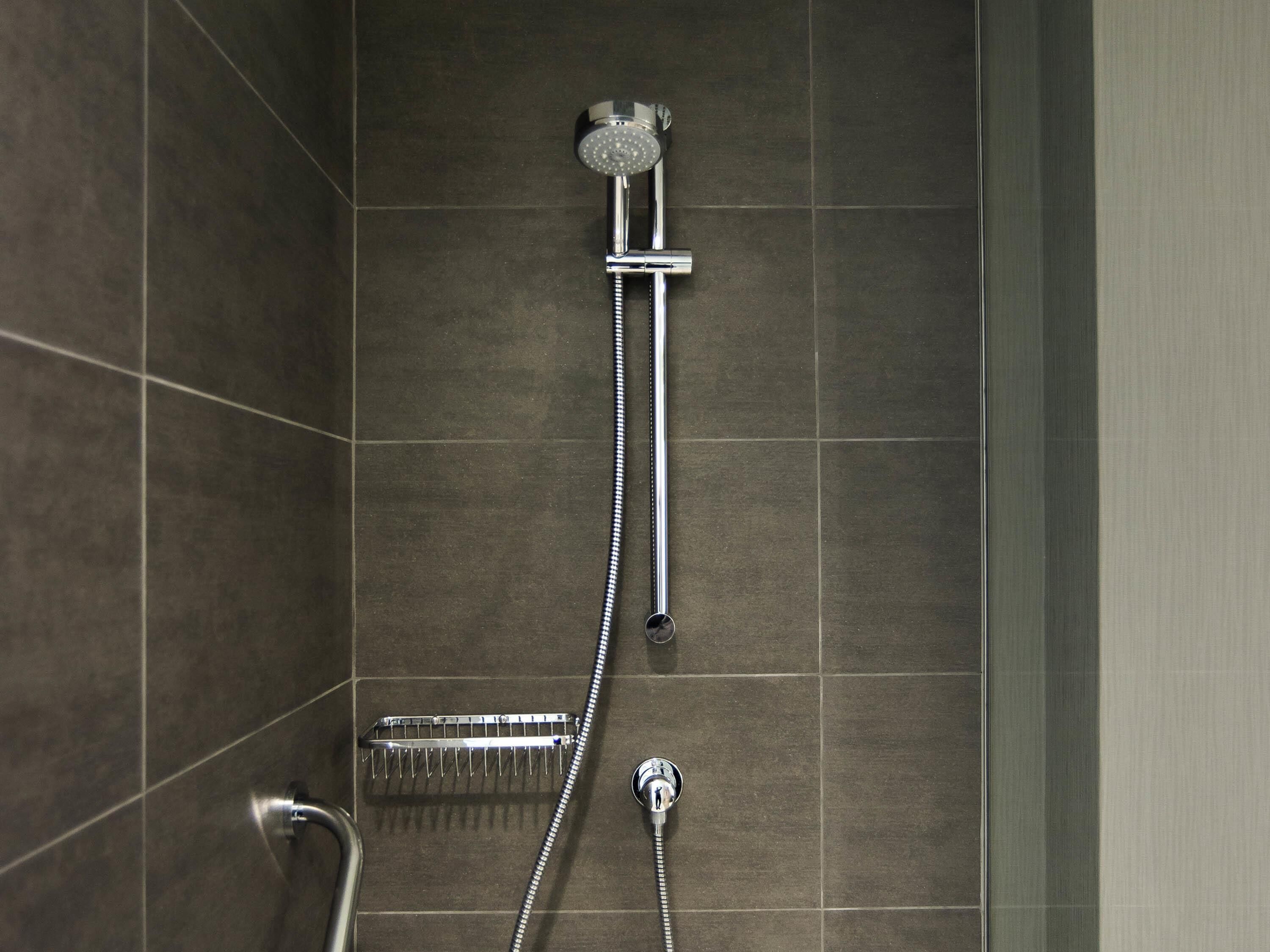 A shower with a handheld hose and a wall-mounted showerhead in a tiled bathroom.