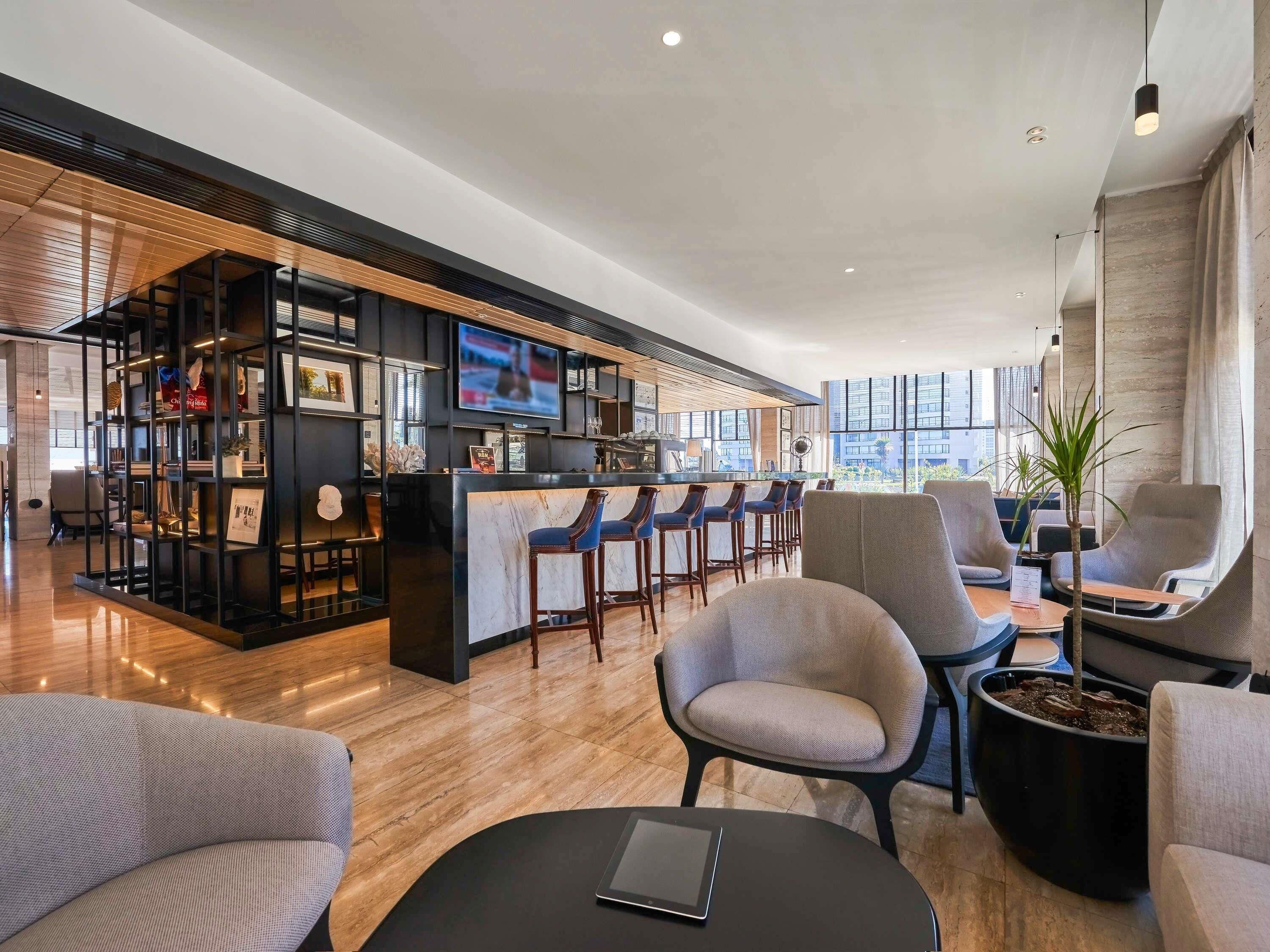 Un espace bar moderne doté d’un téléviseur, de tabourets de bar et d’un coin salon avec des chaises et une table.