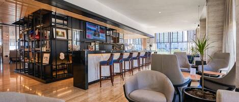 Un espace bar moderne doté d’un téléviseur, de tabourets de bar et d’un coin salon avec des chaises et une table.