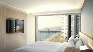 Una habitación de hotel moderna con una cama grande, un televisor y vistas a un puente y una playa.