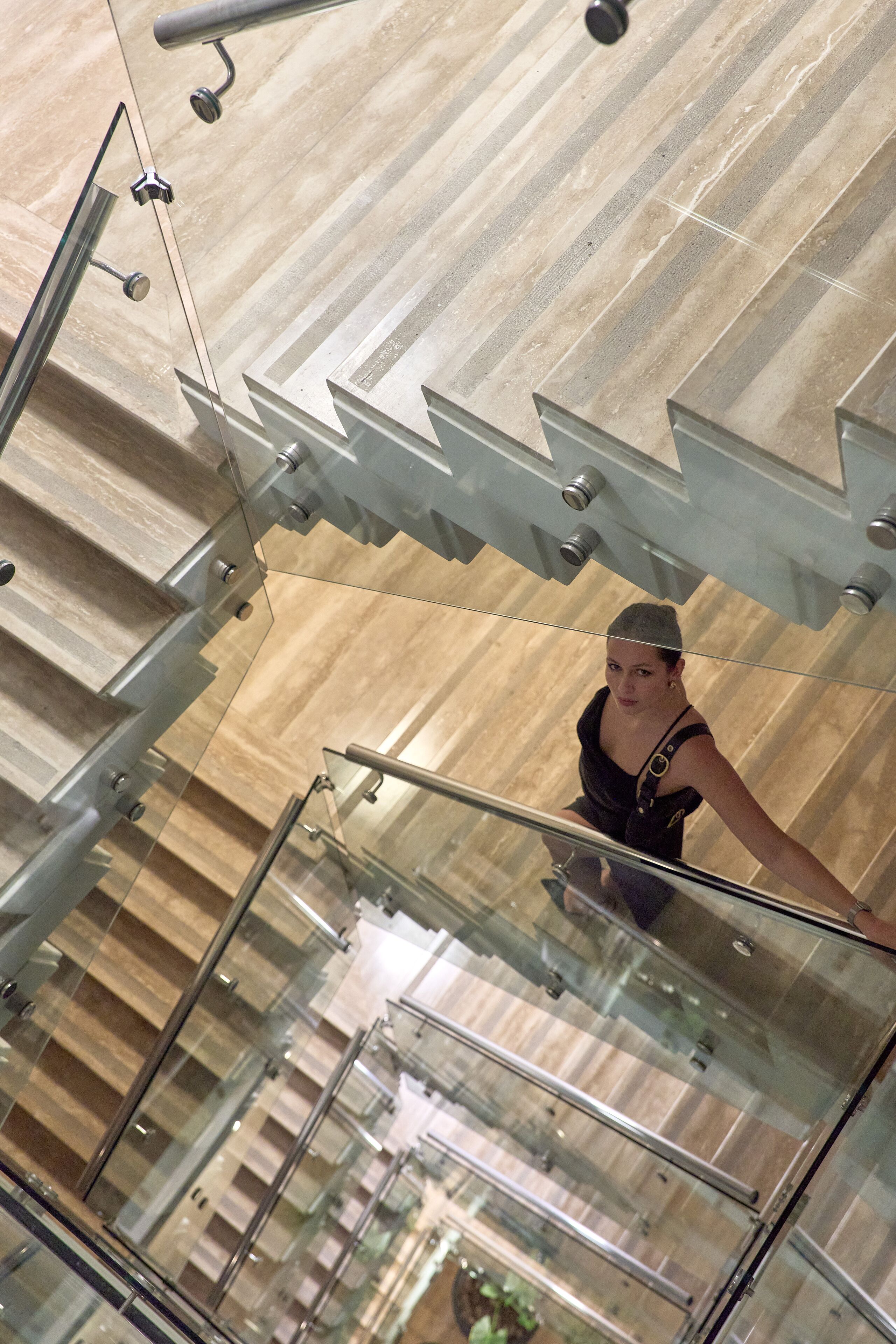 Un intérieur moderne avec une balustrade en verre et une personne descendant un escalier.