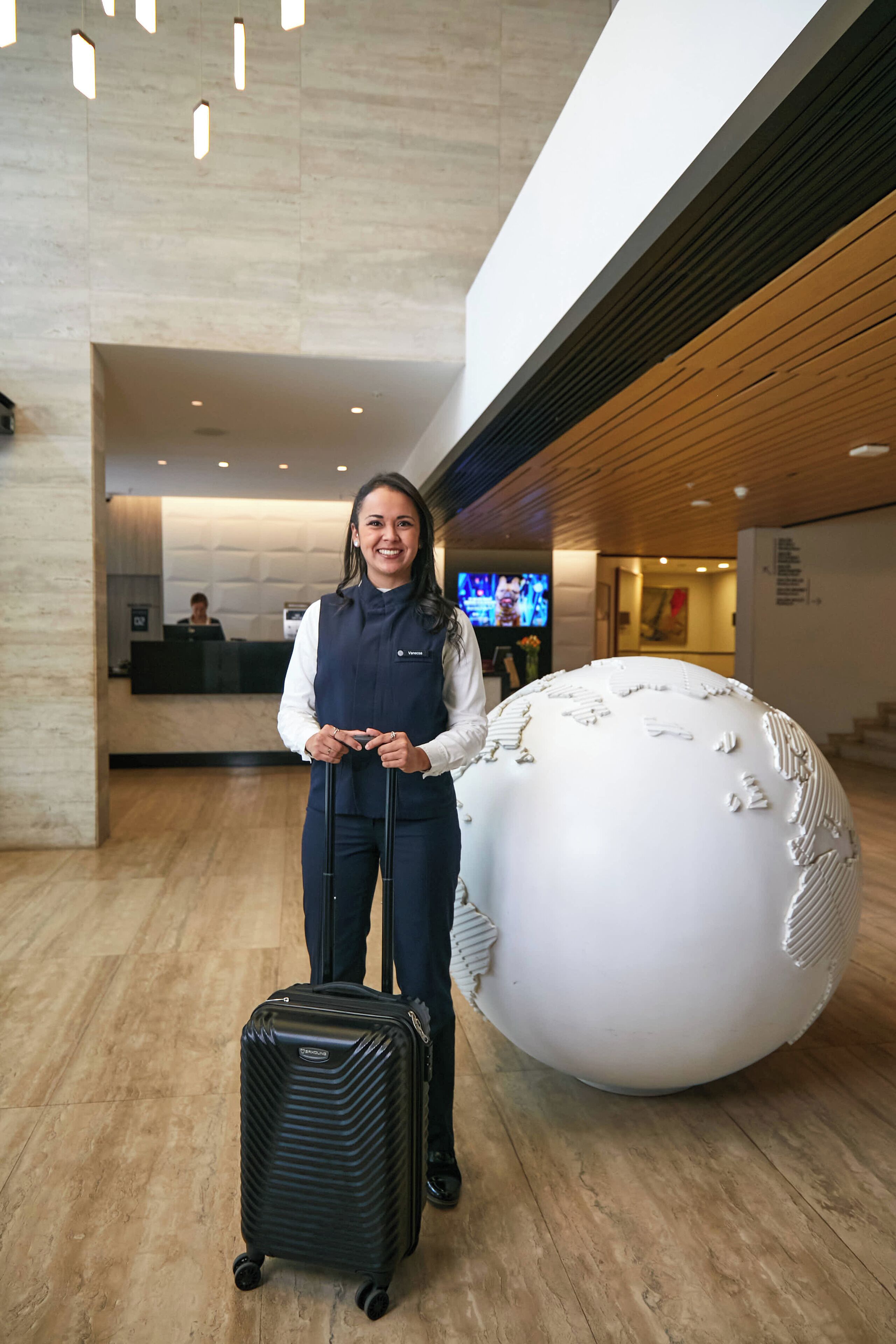 A reception area with a receptionist, a large white spherical sculpture, and a black suitcase.