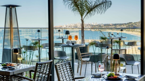 Un restaurante con terraza al aire libre con vistas a la playa y al paisaje urbano.