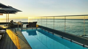 Zona junto a la piscina con sillones y sombrillas, con vistas al mar.