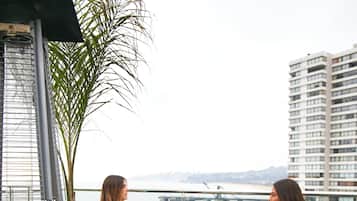 Dos personas sentadas en una mesa en un balcón con vista a una playa y un puente.