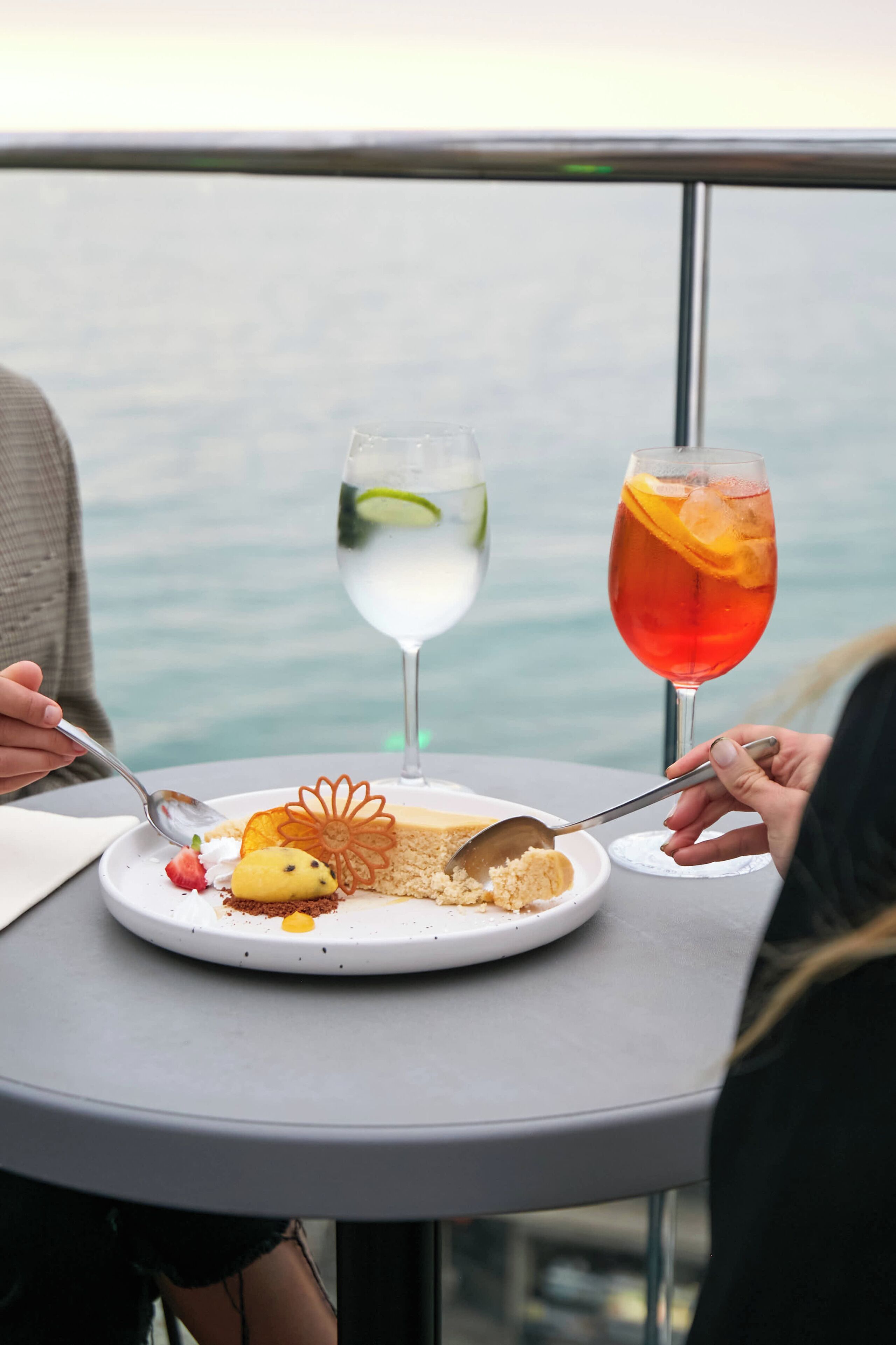 A dining table with a plate of food and two drinks, overlooking a body of water.