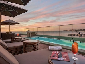Área de piscina com espreguiçadeiras, mesa de vidro e uma revista.