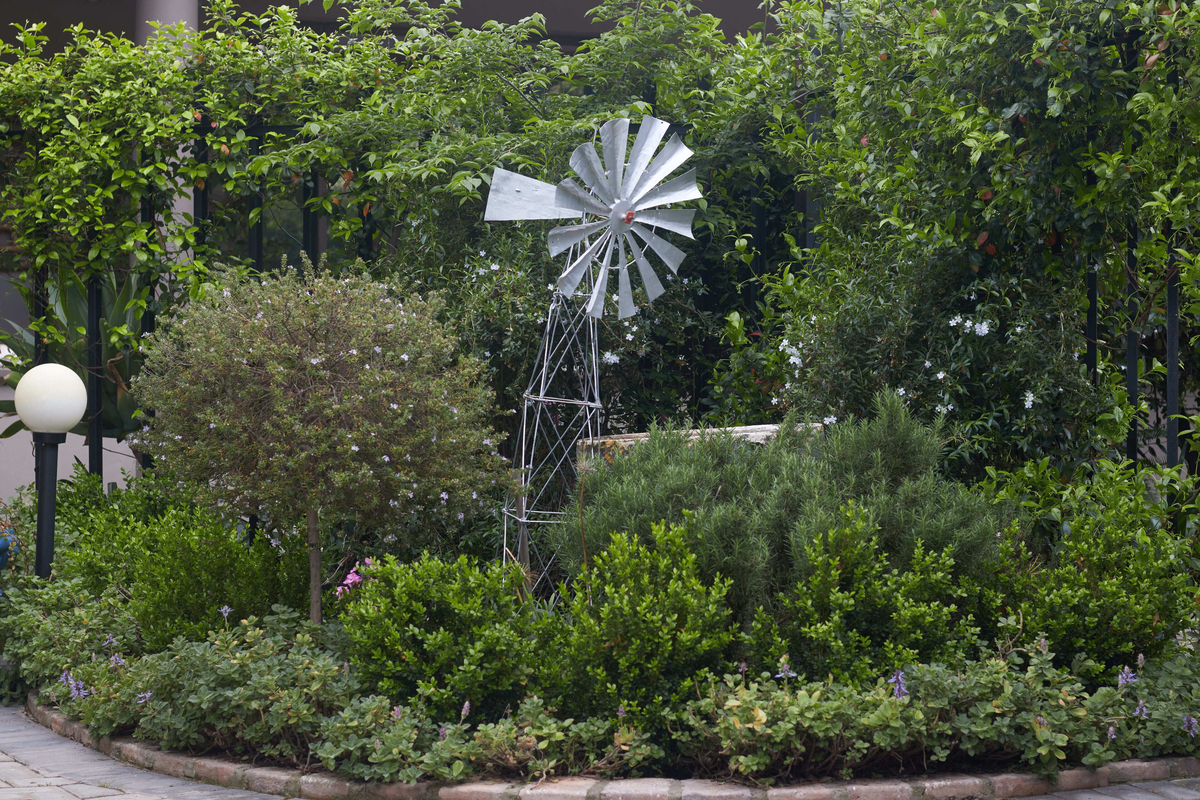 A windmill surrounded by lush greenery and a lamp post.