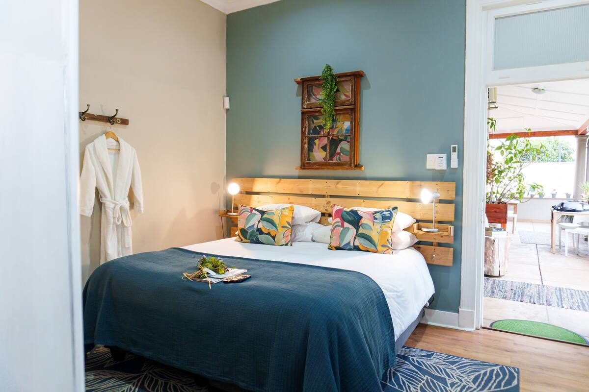 A bedroom with a bed, bedside tables, a hanging plant, and a view of the outside.