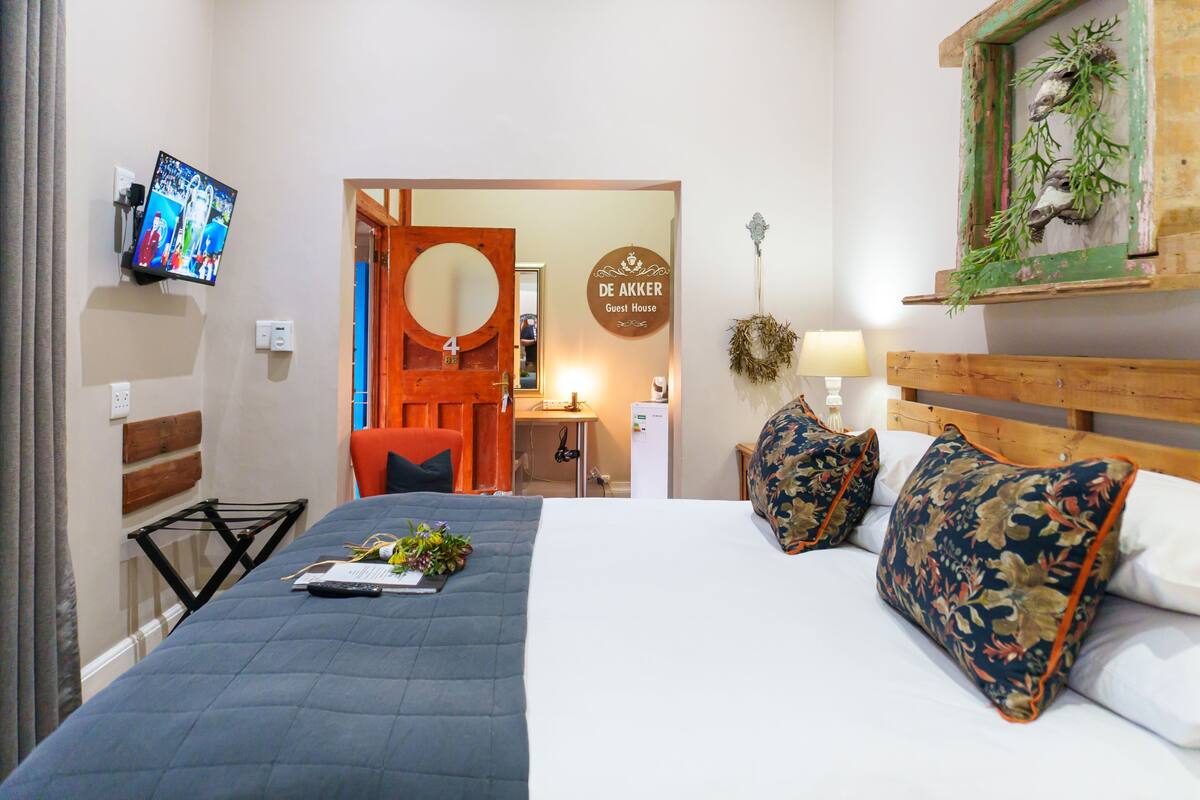 A hotel room with a bed, a TV, a desk, and a sign indicating it's a guest house.