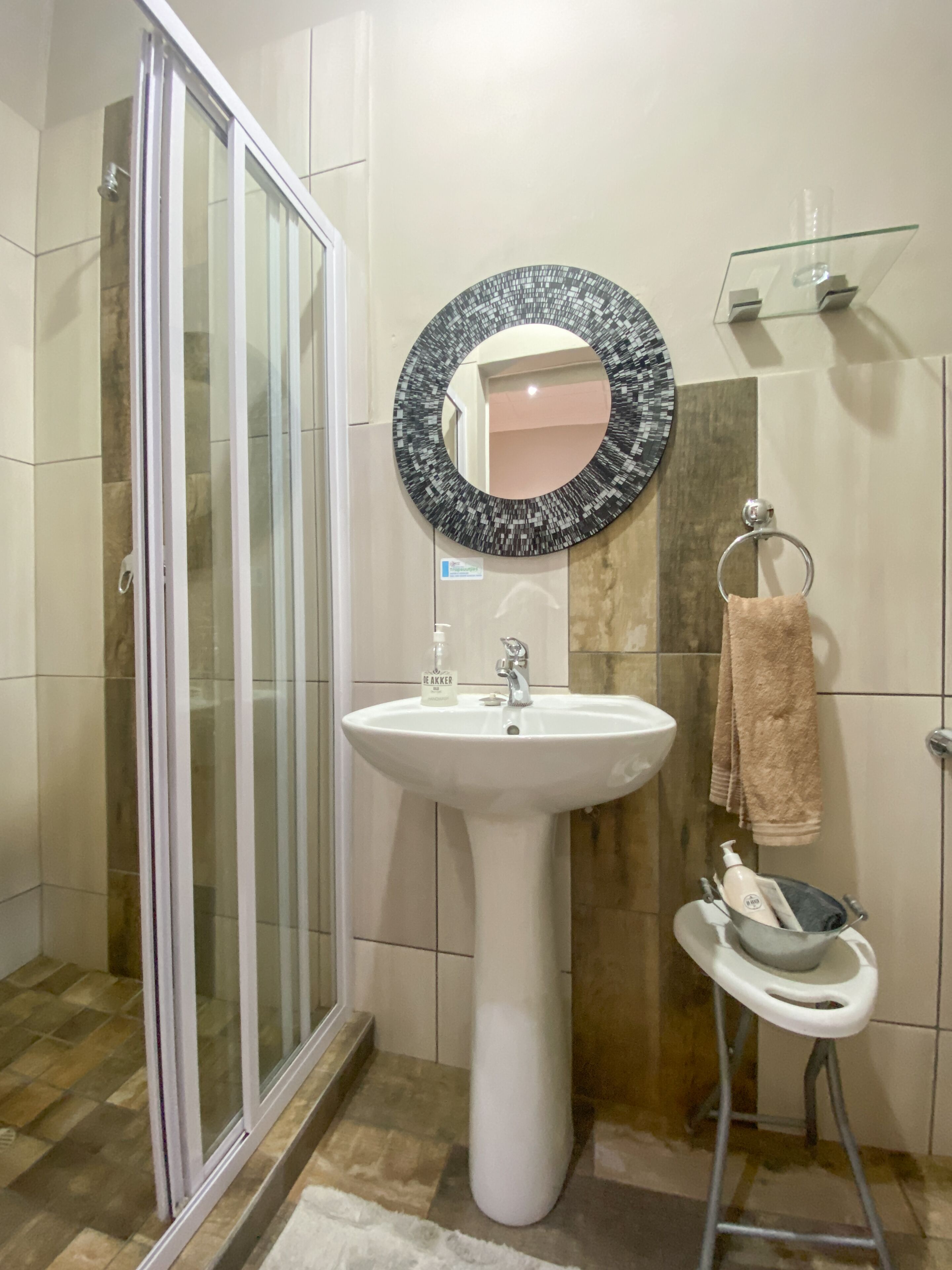 A bathroom with a glass shower door, a white sink, a round mirror, and a towel rack.