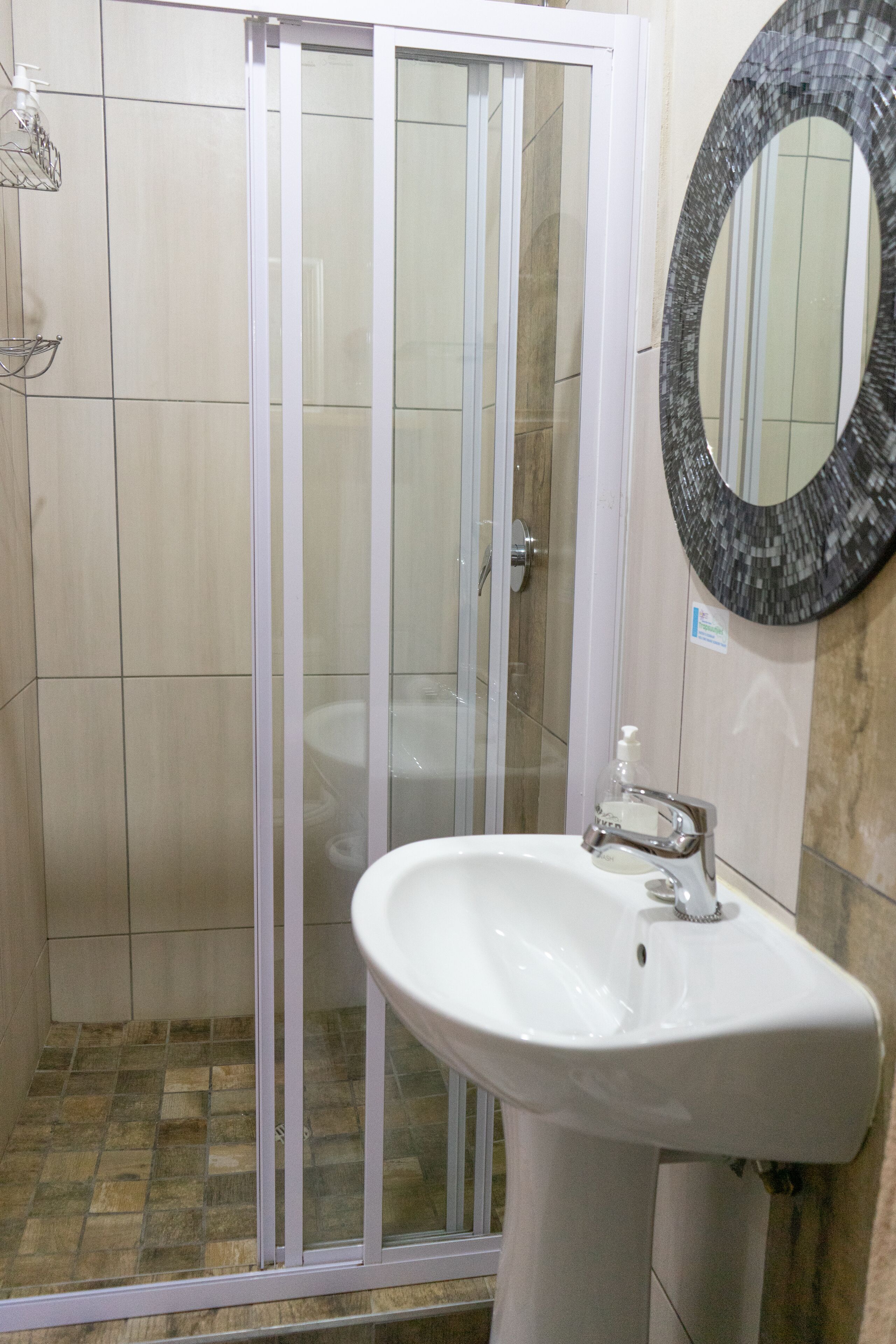 Une salle de bain dotée d’une douche à parois de verre, d’un lavabo blanc et d’un miroir en mosaïque.