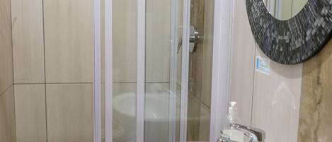 Une salle de bain dotée d’une douche à parois de verre, d’un lavabo blanc et d’un miroir en mosaïque.