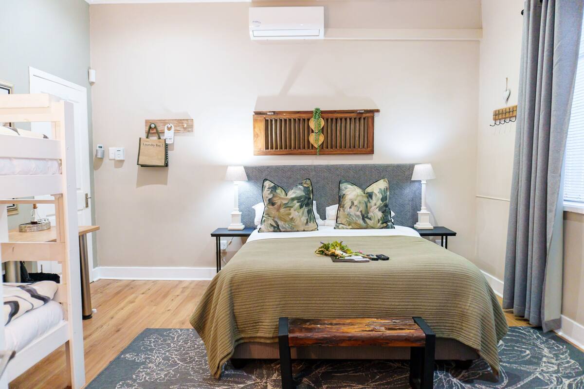 A bedroom with a bed, bedside tables, a bench, a wall-mounted air conditioner, a wall-mounted shelf, and a hanging light fixture.