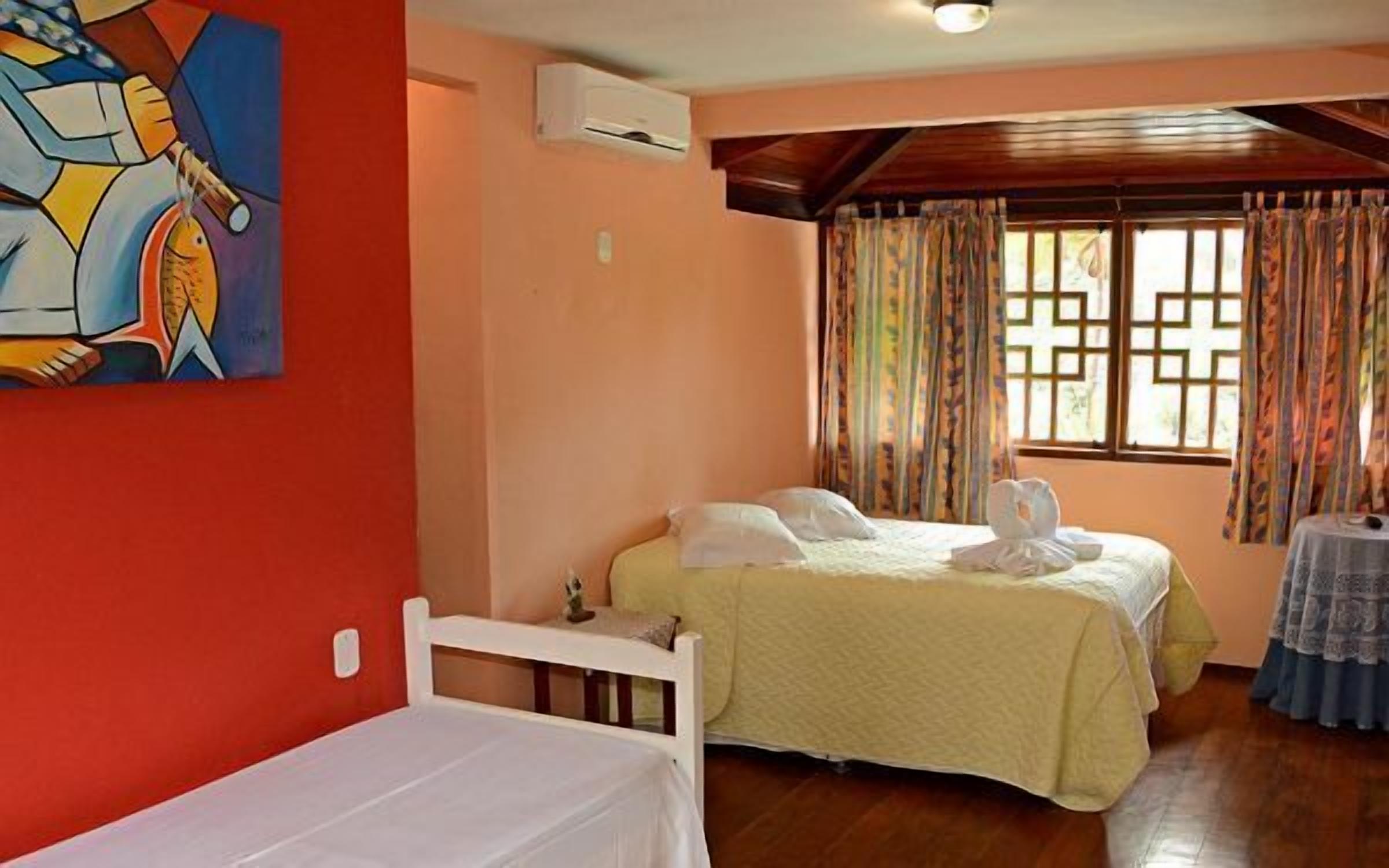 A room with two beds, a painting on the wall, an air conditioning unit, and a window with curtains.