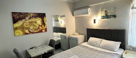 Une chambre moderne avec un grand lit, un bureau et une chaise. On y trouve deux unités de climatisation au mur, un tableau et une fenêtre avec des rideaux.