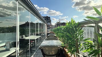 Um terraço no telhado com paredes de vidro, área de estar externa e plantas em vasos.