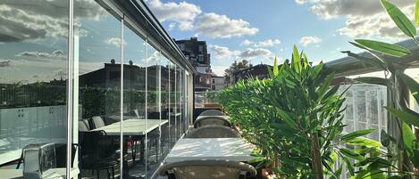 A rooftop terrace with glass walls, outdoor seating, and potted plants.