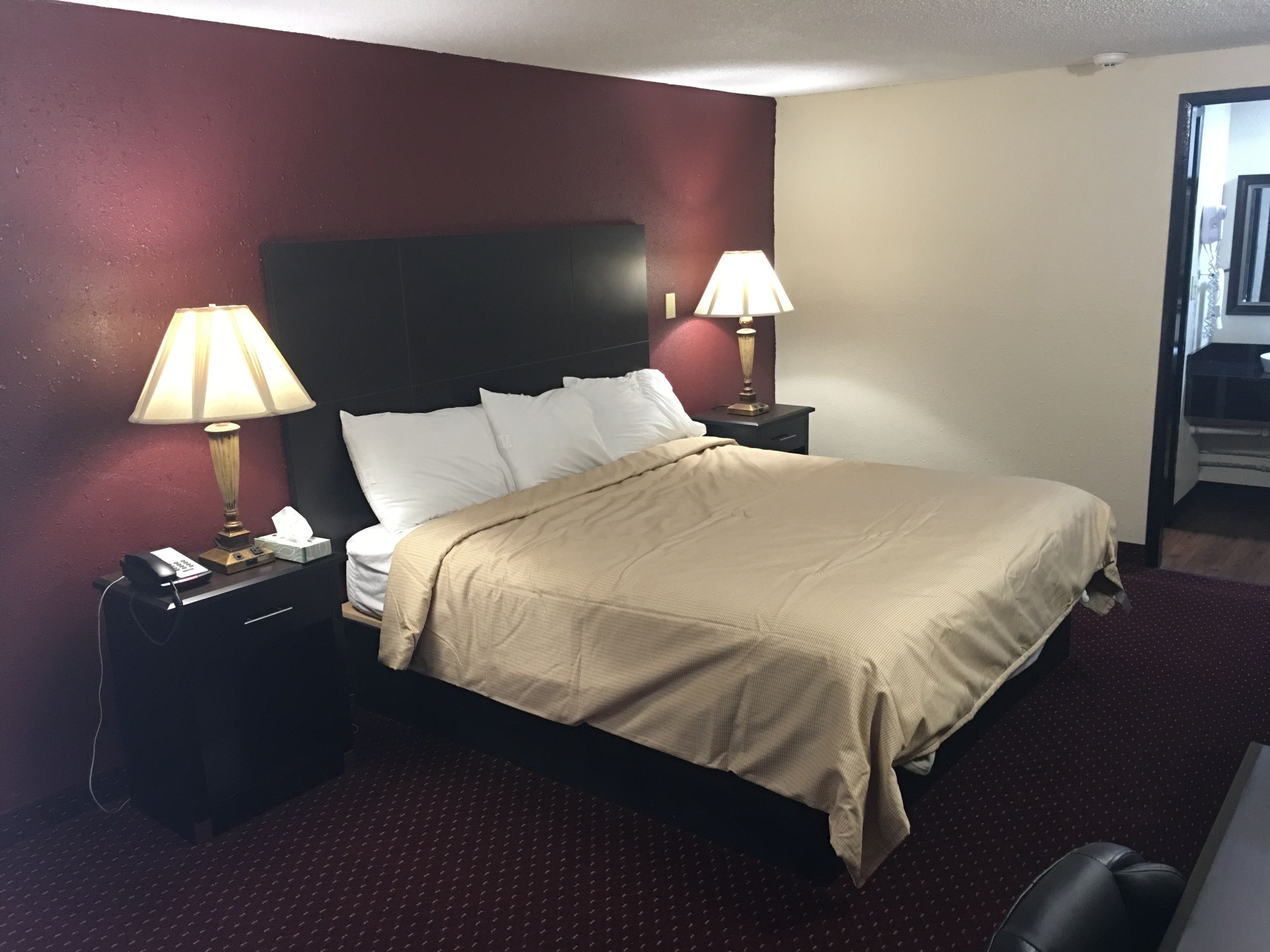 A hotel room with a bed, two bedside lamps, a nightstand with a phone, and a chair.