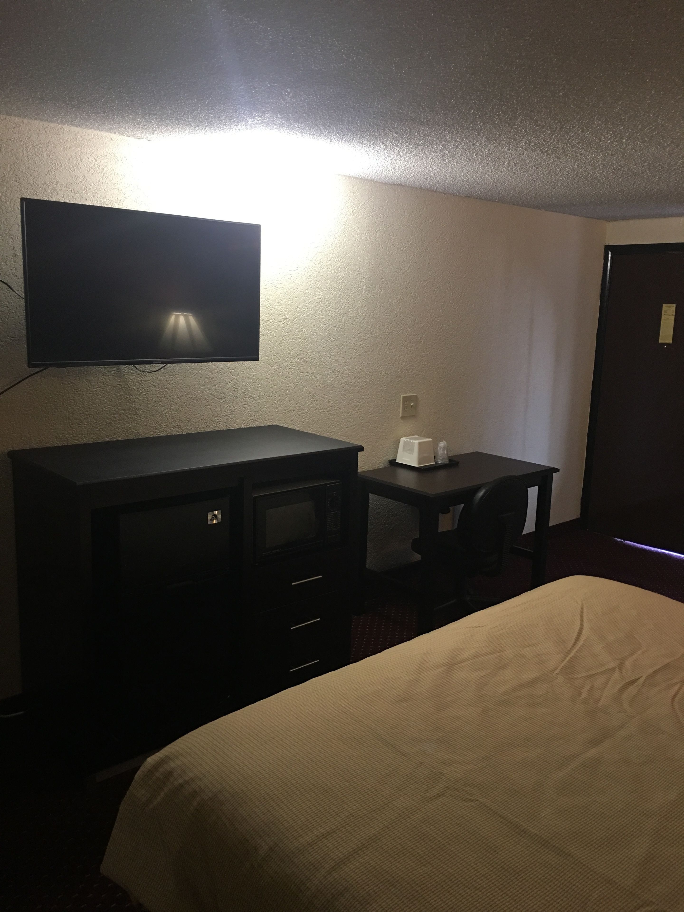 Una habitación de hotel con una cama, un televisor montado en la pared, un escritorio pequeño y un microondas.