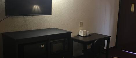 Una habitación de hotel con una cama, un televisor montado en la pared, un escritorio pequeño y un microondas.