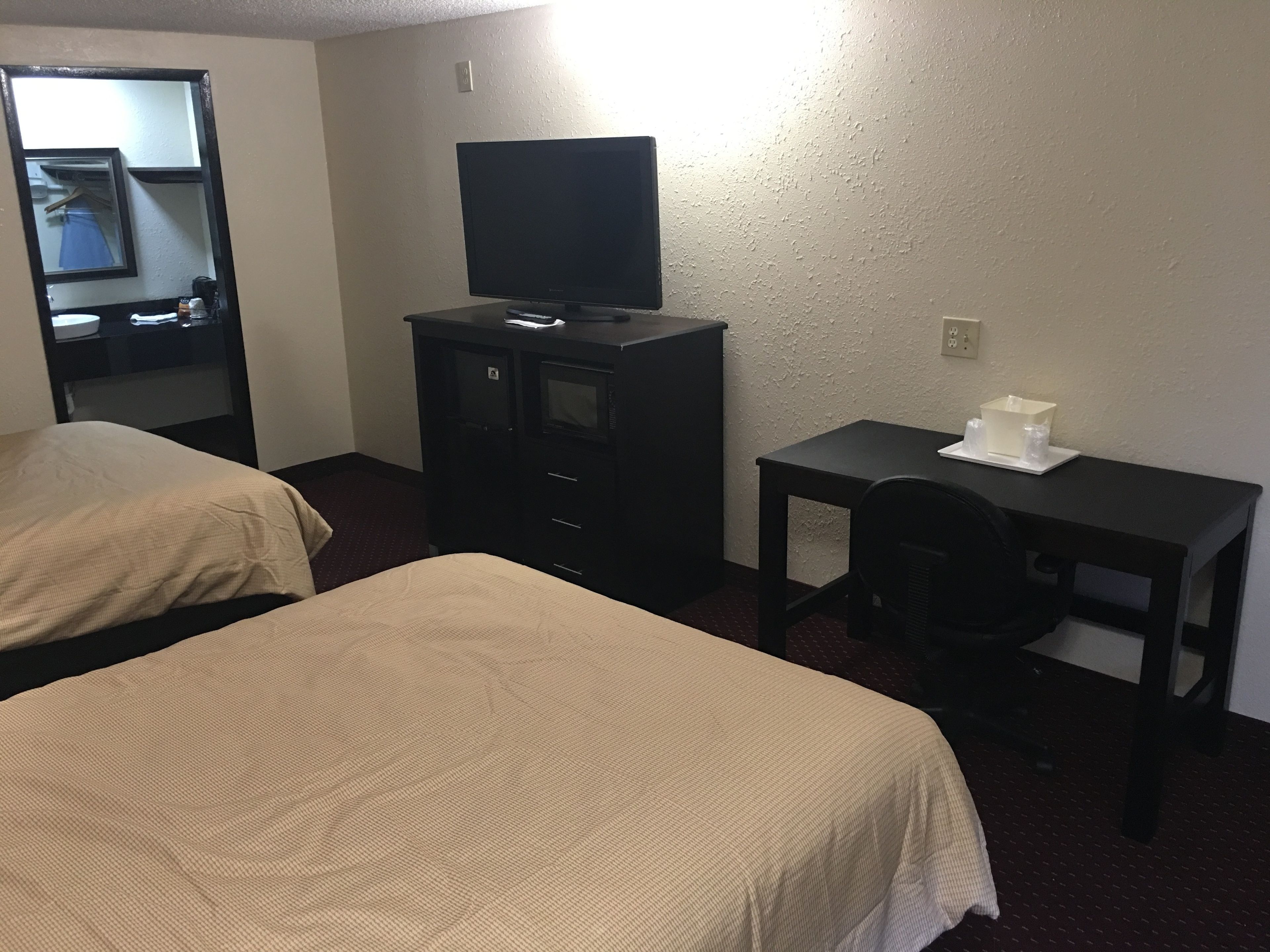 Ein Hotelzimmer mit zwei Betten, einem Schreibtisch, einem Stuhl, einem Fernseher und einem kleinen Tisch mit einer Taschentuchbox.