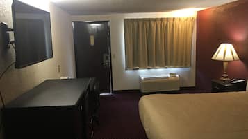 Une chambre d’hôtel équipée d’un lit, d’un bureau, d’une télévision, d’une porte, d’un climatiseur et d’une fenêtre avec des rideaux.