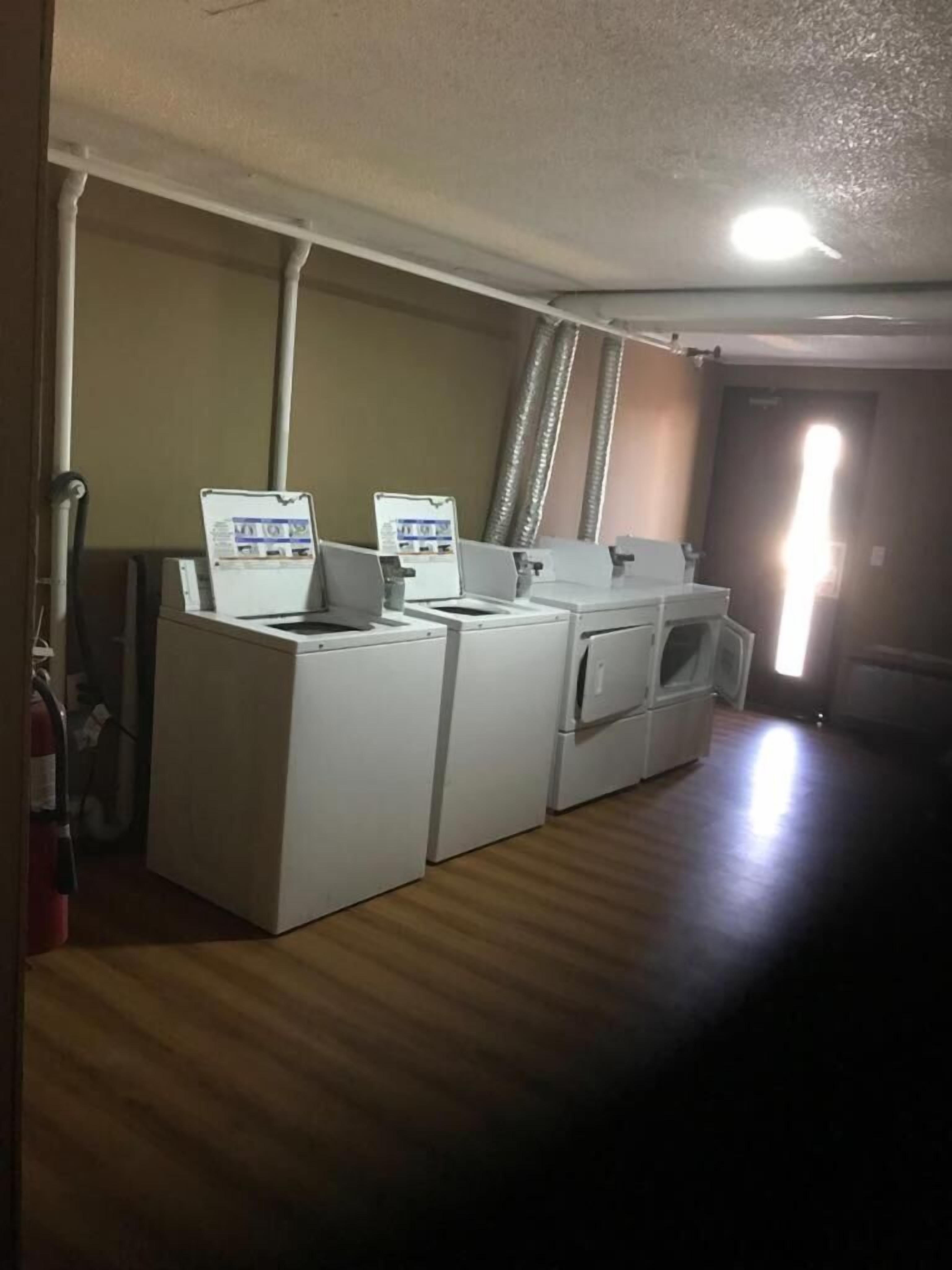Un lavadero con tres lavadoras y secadoras, un techo blanco y una puerta que da a otra habitación.
