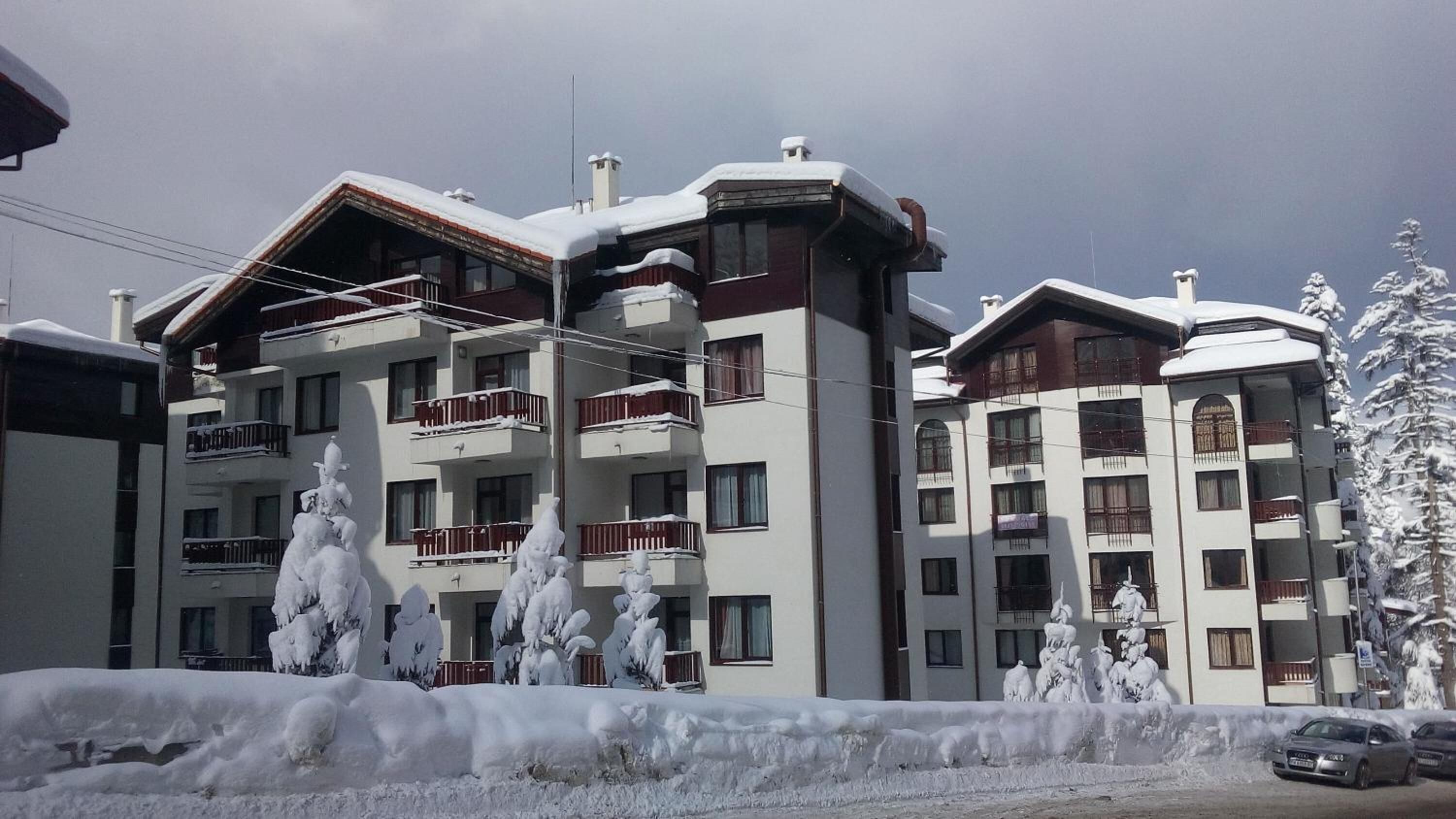 A multi-story hotel with balconies, snow-covered trees, and a clear sky.