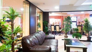 A lobby with a leather sofa, a glass coffee table, and potted plants. - Apart Hotel Flora Residence (Samokov)