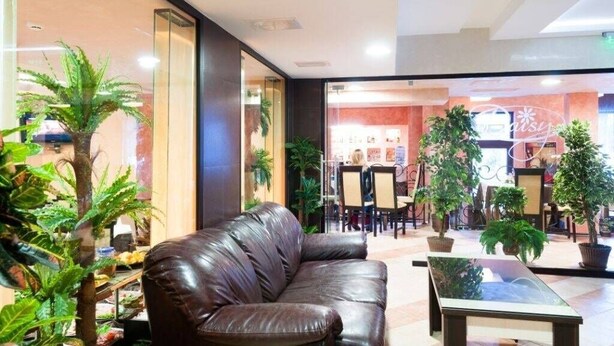 A lobby with a leather sofa, a glass coffee table, and potted plants. - Apart Hotel Flora Residence (Samokov)