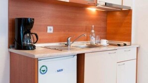 A compact kitchen with wooden cabinets, a built-in sink, and a coffee maker. - Apart Hotel Flora Residence (Samokov)