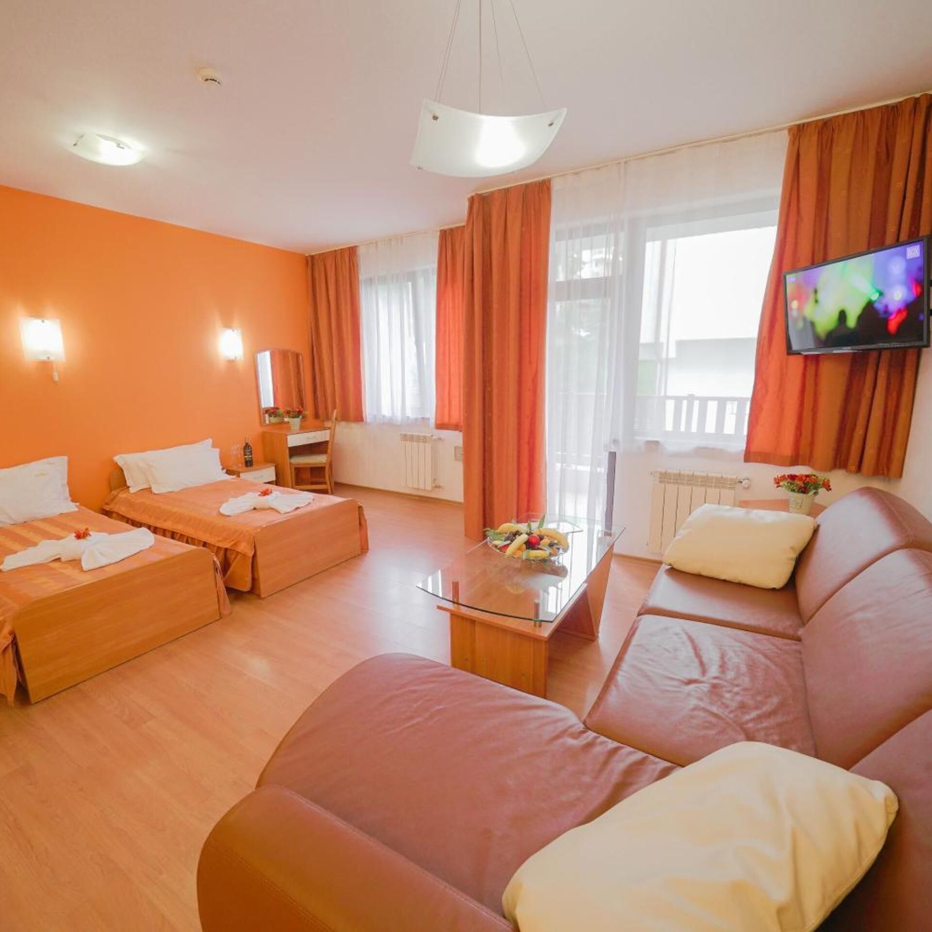 A hotel room with two single beds, a sofa, a coffee table, a TV, and a balcony with curtains.