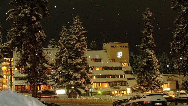 A snow-covered parking lot with cars and a building with illuminated windows. - Hotel Ela (Samokov)