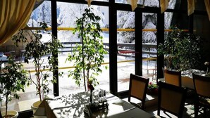 A restaurant with large windows, indoor plants, and a view of a snowy outdoor area. - Hotel Ela (Samokov)