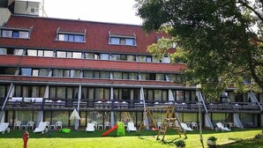 A hotel with a red-tiled roof, multiple balconies, and a grassy courtyard with outdoor seating and a children's play area. - Hotel Ela (Samokov)