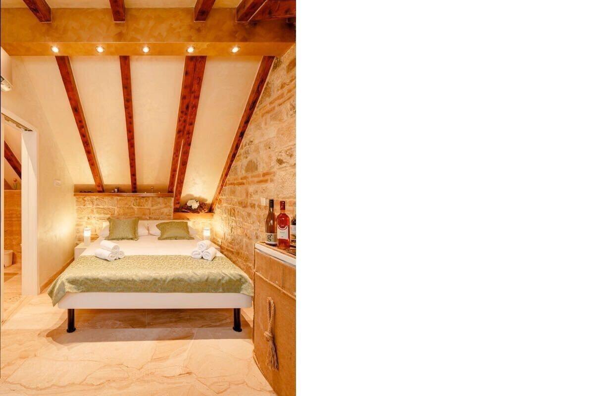 A bedroom with a bed, a nightstand, a stone wall, and a wooden ceiling.