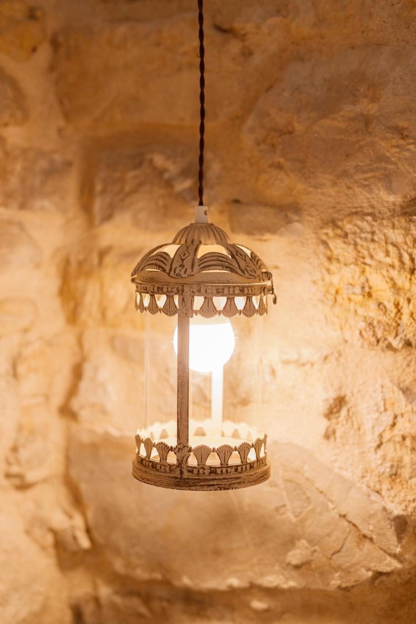 A hanging lantern with intricate designs, suspended in a stone-walled room.