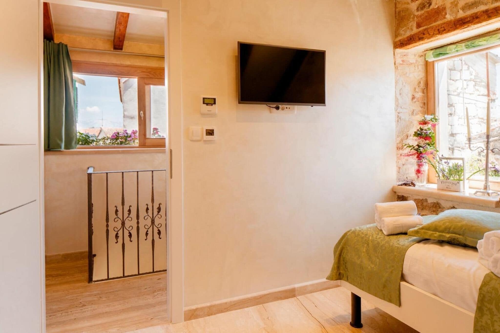 A bedroom with a bed, a TV mounted on the wall, a window with a view, and a door leading to another room.