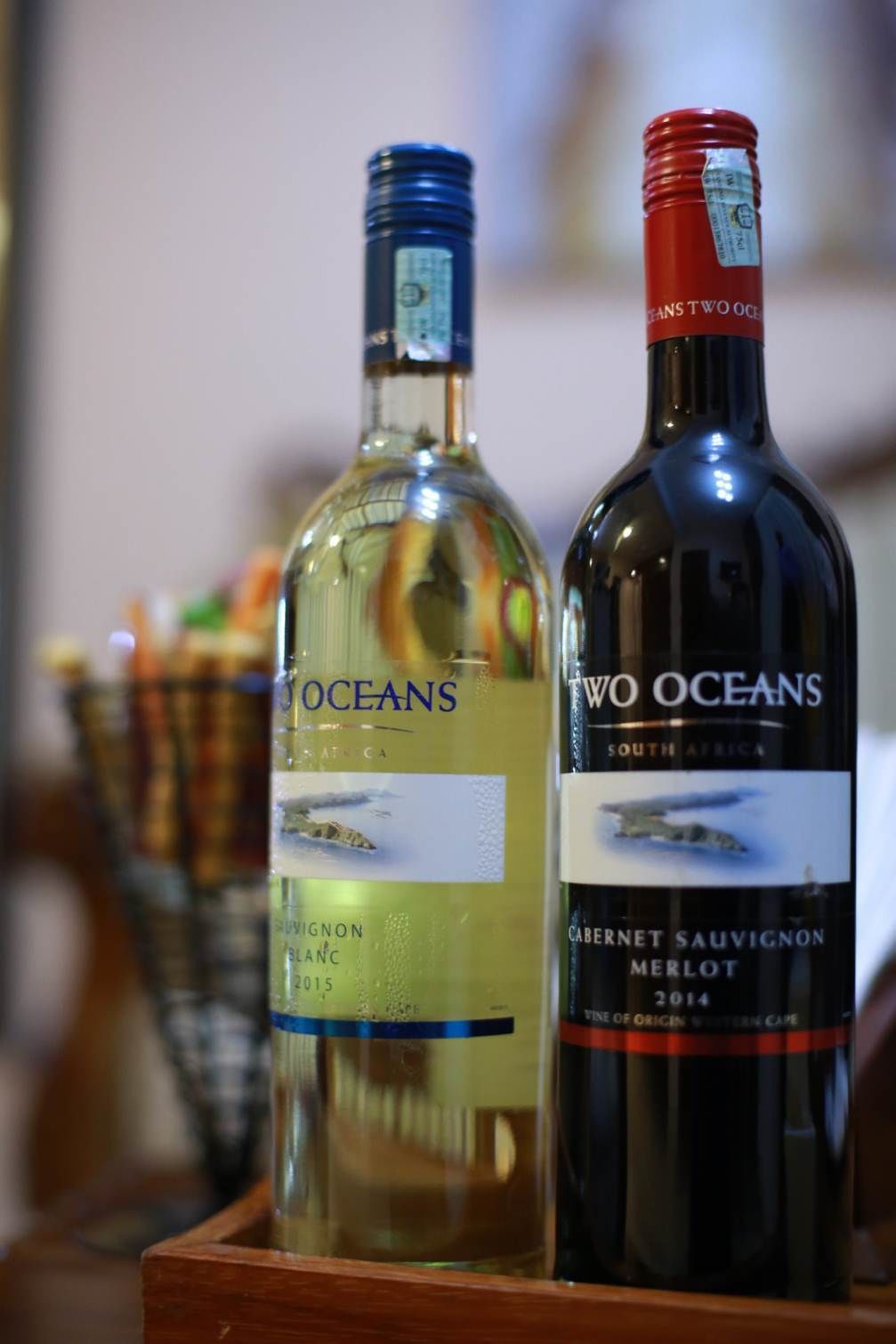 Två flaskor vin, varav den ena är märkt med texten ”Oceans” och den andra med ”Two Oceans”, står på en träyta.