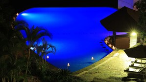 A nighttime view of a resort pool with a blue-lit water feature, surrounded by palm trees and lounge chairs. - Malaika Beach Resort (Mwanza)