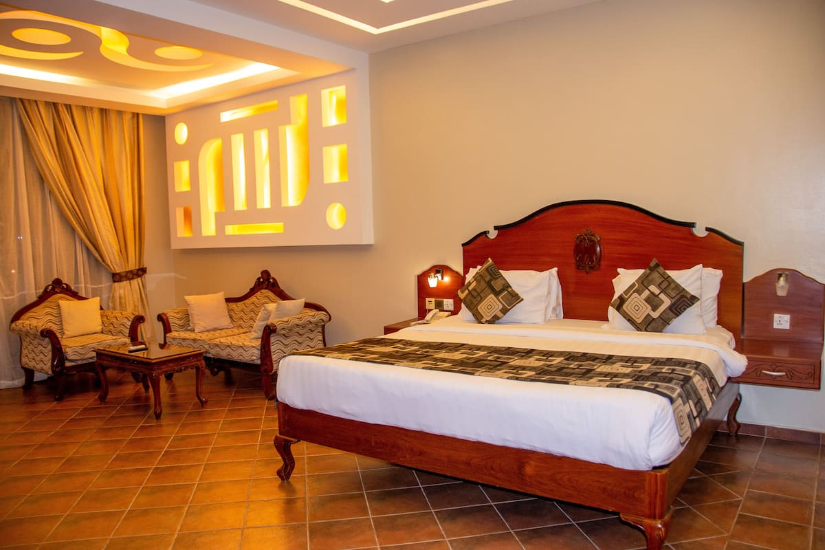 Una habitación de hotel con una cama grande, dos sillones, una mesita y un televisor instalado en la pared.