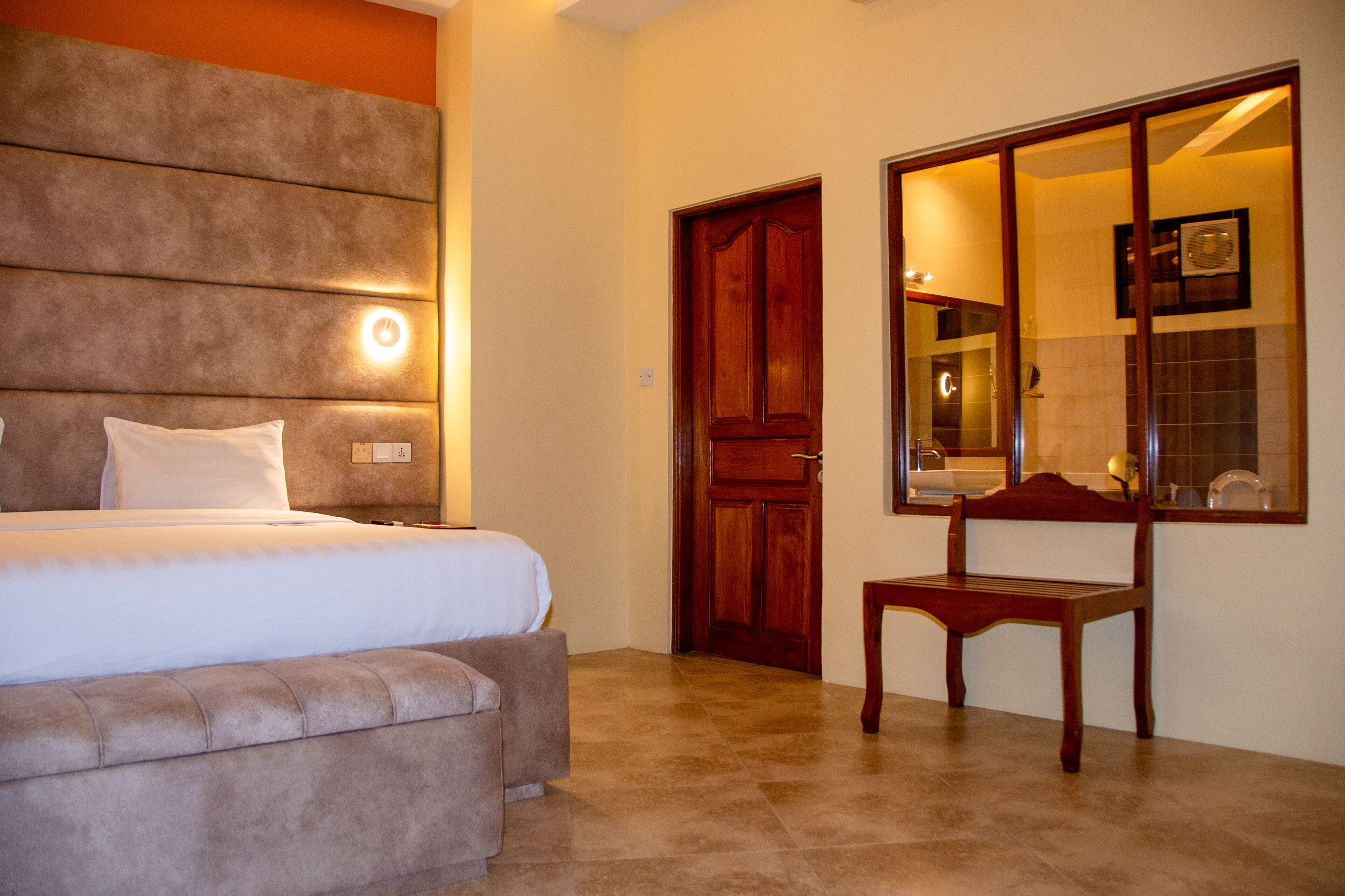 Un dormitorio con cama, un banco, una puerta de madera y un espejo.