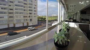 Blick vom Hotelzimmerfenster auf ein mehrstöckiges Gebäude, eine Straße mit Fahrzeugen und eine grüne Landschaft.