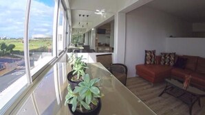 Ein modernes Wohnzimmer mit Glastisch, Topfpflanzen, einem roten Sofa und Blick auf eine Stadtlandschaft durch große Fenster.