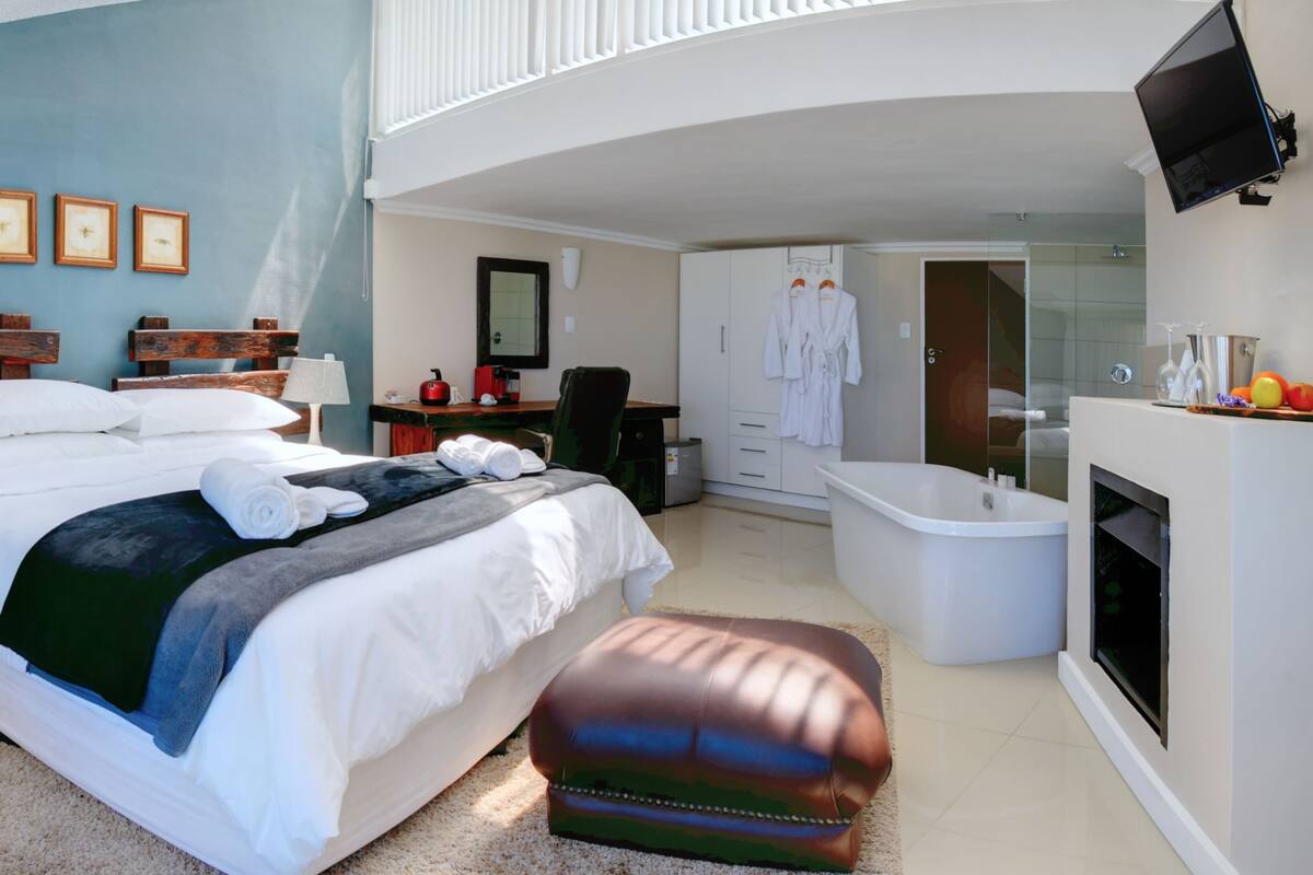 A modern hotel room with a large bed, a desk, a chair, a bathroom with a bathtub, and a TV mounted on the wall.