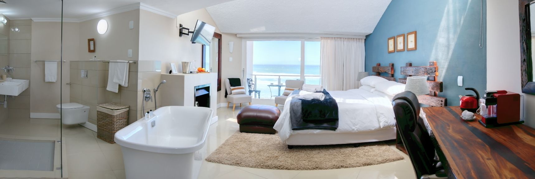 Ein modernes Hotelzimmer mit einem großen Bett, einer Sitzecke, einem Badezimmer mit Badewanne und Meerblick.