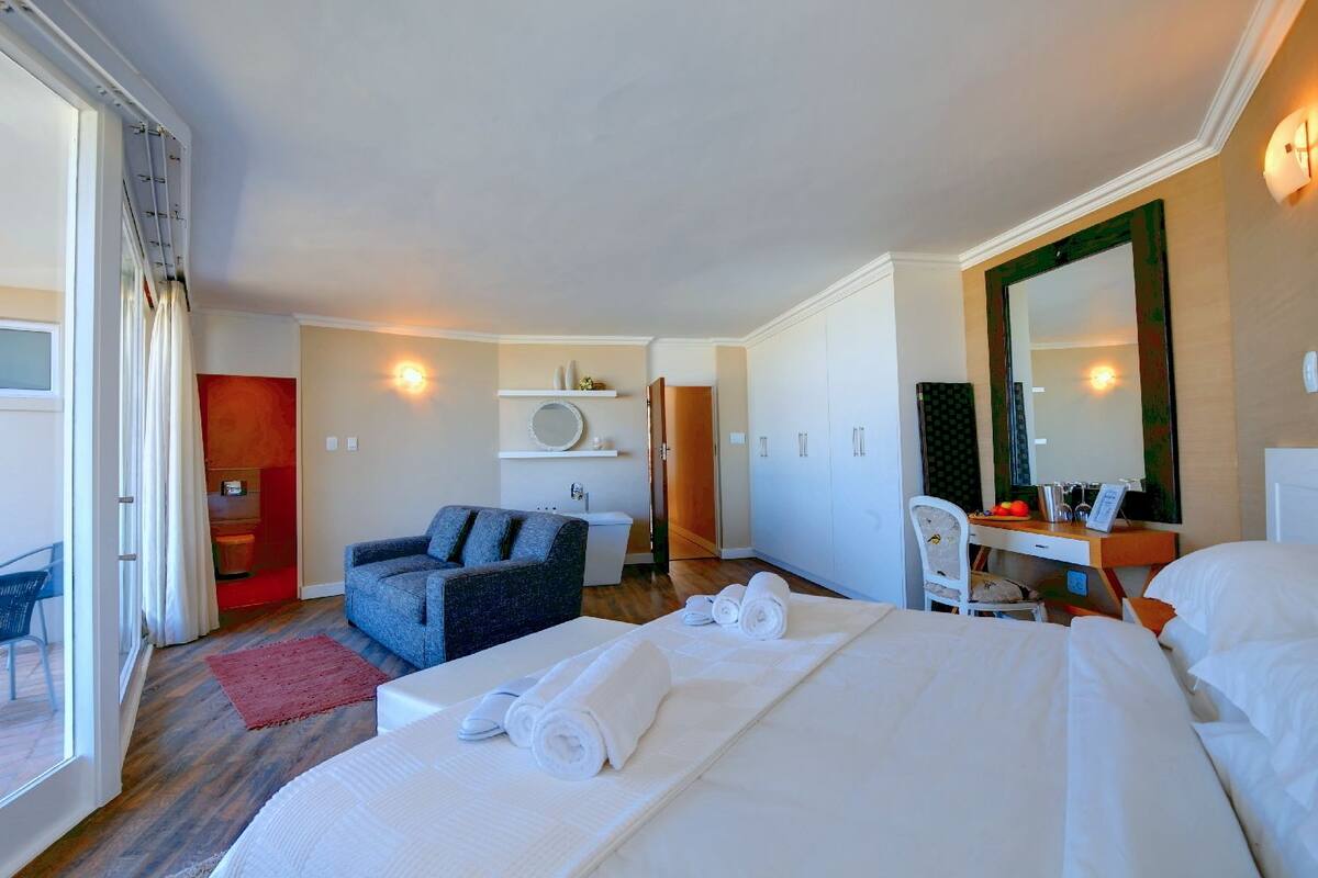 A hotel room with a large bed, a sofa, a desk with a mirror, and a bathroom visible through an open door.